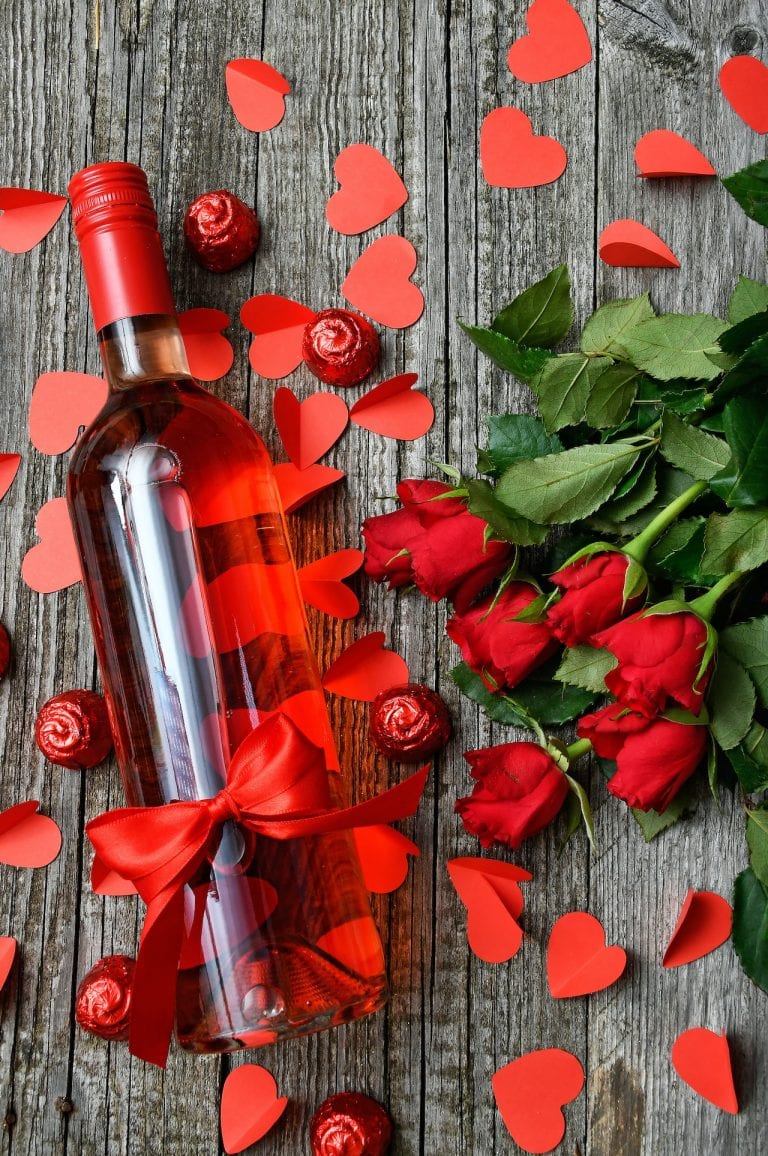 Valentinstag Flat Lay auf altem Holztisch mit Rotweinflasche und Rosen